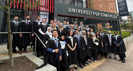 A large group of Strathclyde Business School graduates wearing academic gowns pose on steps outside the University of Strathclyde building in Glasgow